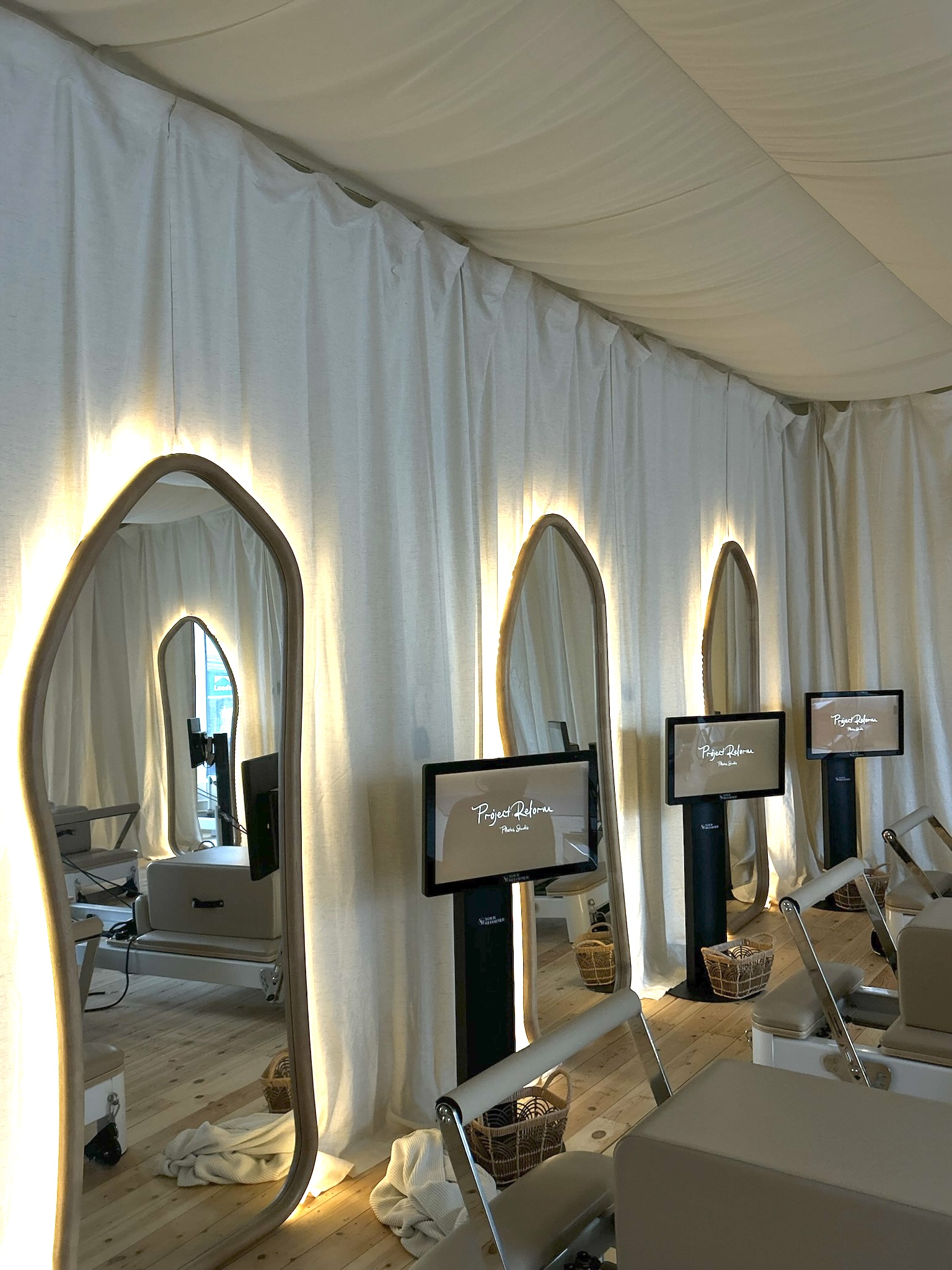 Reformer stations with individual screens beside the studio mirrors